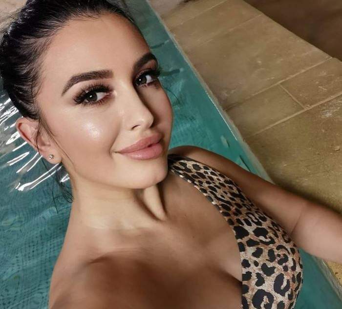 Mirela Banias se află în piscină. Bruneta are părul prins în coc și poartă un costum de baie cu animal print, stil leopard.