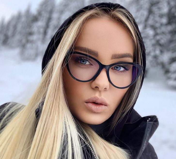 Maria Constantin se află afară, în zăpadă. Artista poartă ochelari de vedere și un hanorac negru, având gluga pe cap.