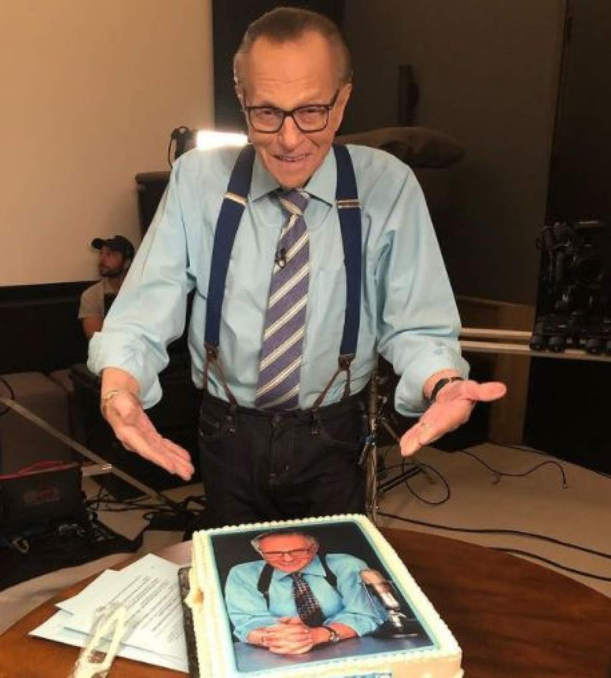Larry King, îmbrăcat ân albastru ți negru își prezintă tortul cu imaginea sa