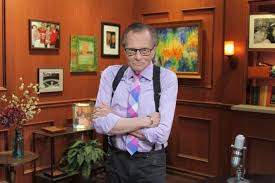 Larry King, cu mâinile încrușișate la piept, într-o cameră plină de tablouri