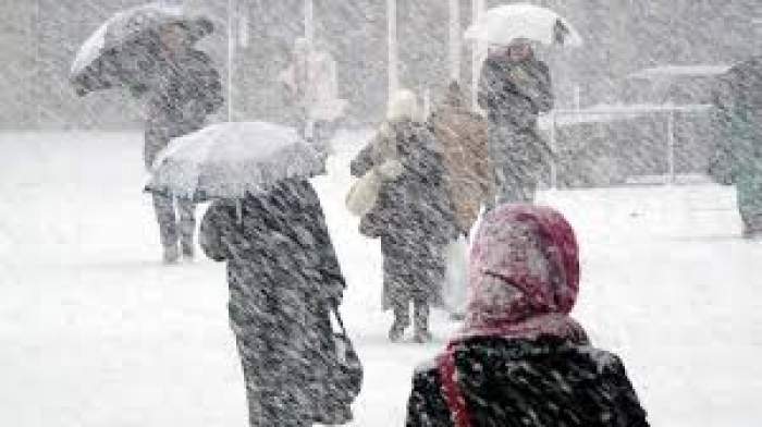 Mai multe persoane merg prin zăpadă, cu umbrelele deschise