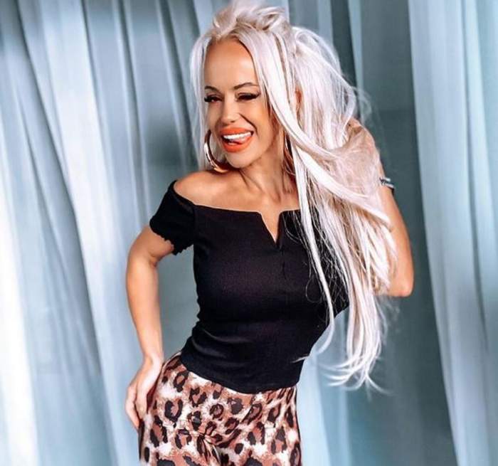 Anda Adam e îmbrăcată în colanți cu animal print, tip leopard, și un tricou negru. Vedeta zâmbește larg și își ține o mână pe posterior și una prin păr.