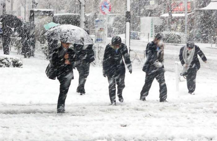 Oameni fotografiați în oraș, pe ninsoare, cu umbrele în mână