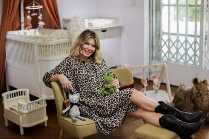 Gina Pistol, în ținută aniamal print, așezată pe fotoliu, lângă pătuțul fetiței
