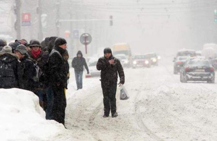 Oameni, îmbrăcați foarte gros, așteptând pe marginea drumului plin de zăpadă