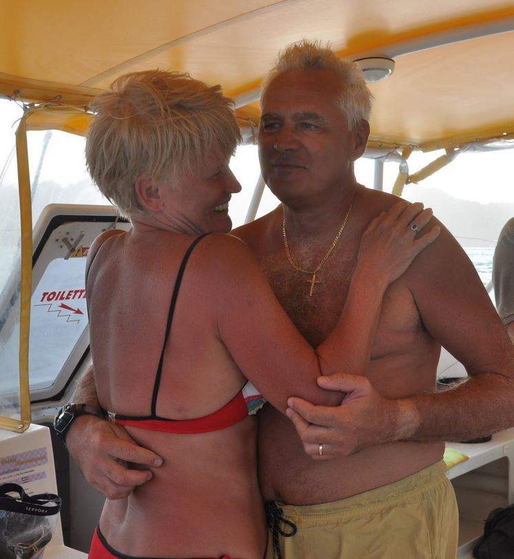 Monica Tatoiu și soțul ei în vacanță. Ea poartă un costum de baie roșu, iar el niște pantaloni scurți galben. Cei doi se țin în brațe.