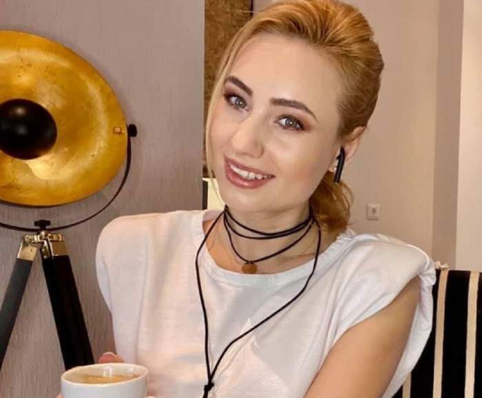 Emilia Dorobanțu poartă un maiou alb. Vedeta ține în mână o ceașcă de cafea albă și zâmbește larg.