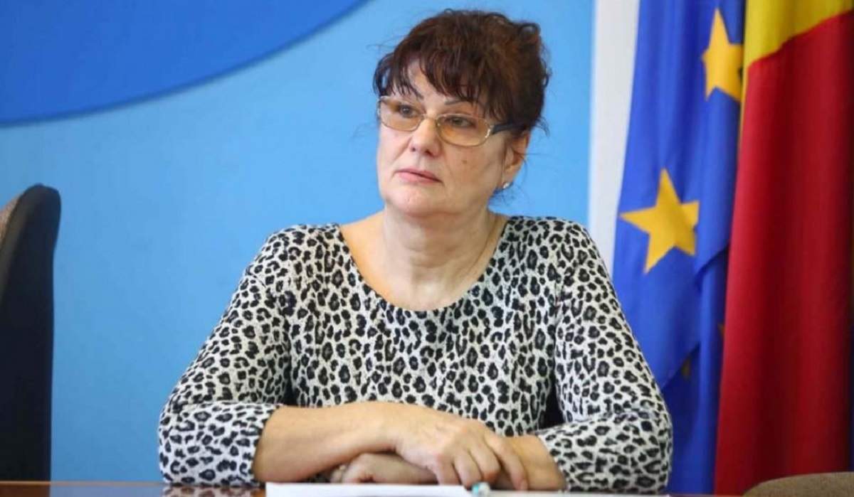 Subprefectul de Timiș, Elena Popa, stă pe scaun și ține brațele unul peste altul pe masă. Femeia poartă ochelari de vedere și are părul prins în coc.