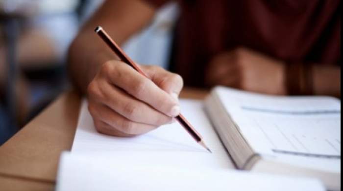 Mâna unei eleve care scrie cu creionul pe o foaie albă