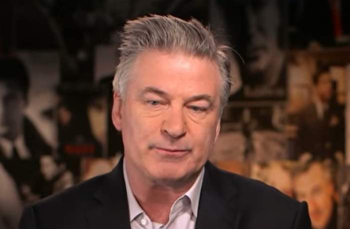 Alec Baldwin, privind în jos, în costum negru