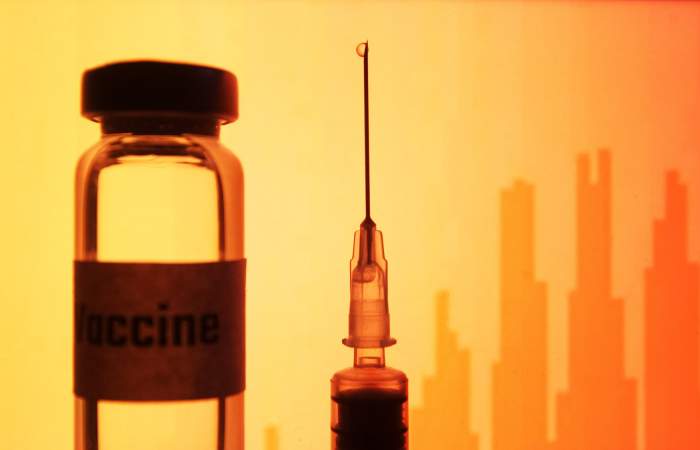 O seringă și o sticlă de vaccin, pe fundal portocaliu