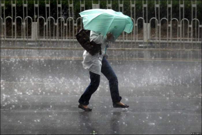 O femeie care merge cu o umbrela verde prin ploaie
