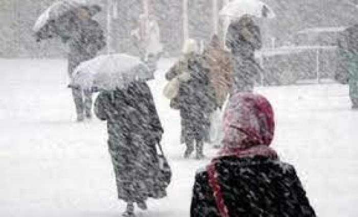 Oameni care merg prin zăpadă, cu umbrelele