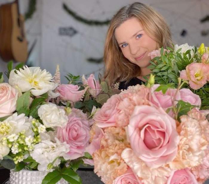 Cristina Ciobănașu e îmbrăcată într-un tricou negru. Artista ține în mâini niște buchete de flori roz și albe.