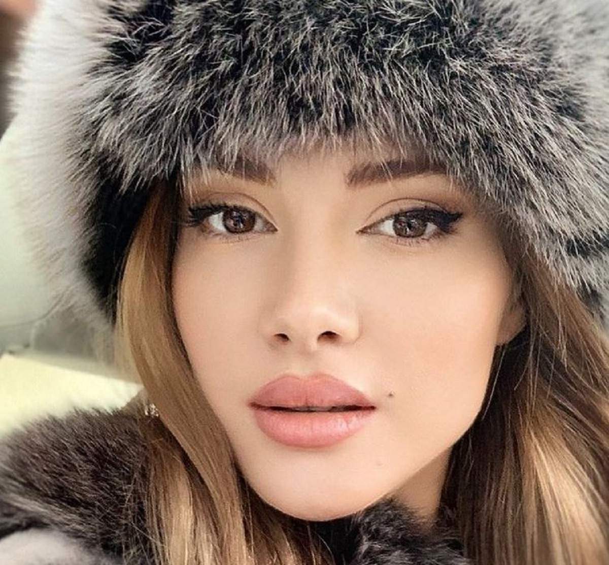 Otilia Bilionera poartă o căciulă și o haină cenușie, ambele articole fiind din blană. Artista își face un selfie