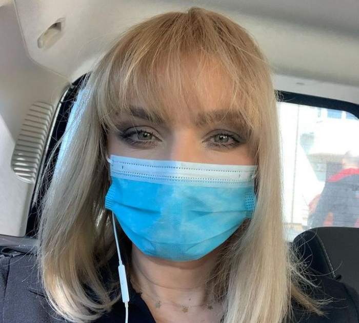 Cristina Cioran este în mașină. Vedeta poartă mască de protecție și are căștile în urechi.
