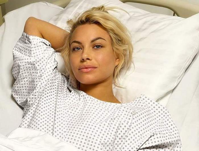 Amna stă întinsă pe patul de spital. Vedeta își ține o mână sub cap și poartă un halat alb.
