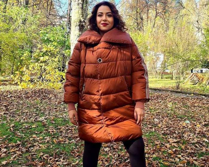 Oana Roman se află în parc. Vedeta poartă o geacă oversized, maro, și pantaloni negri, mulați.