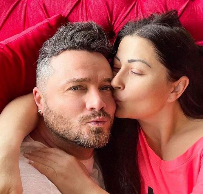 Gabriela Cristea și Tavi Clonda stau pe un fotoliu roșu. Ea poartă un tricou roșu și îl sărută pe obraz, iar el unul alb.