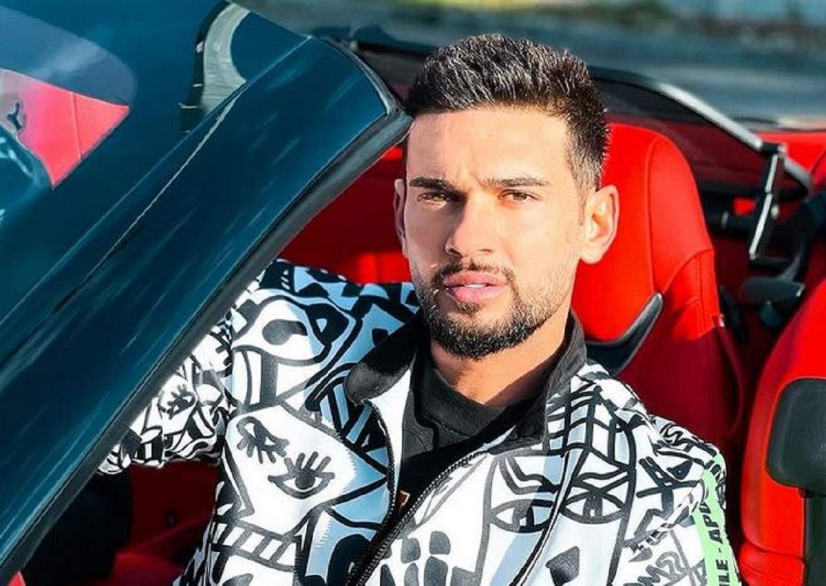 Dorian Popa se află într-o mașină decapotabilă cu tapițerie roșie. Artistul poartă un hanorac alb cu model negru.
