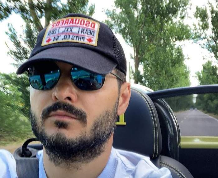 Liviu Vârciu e într-o mașină decapotabilă. Actorul poartă un tricou bleu, ochelari de soare și șapcă.