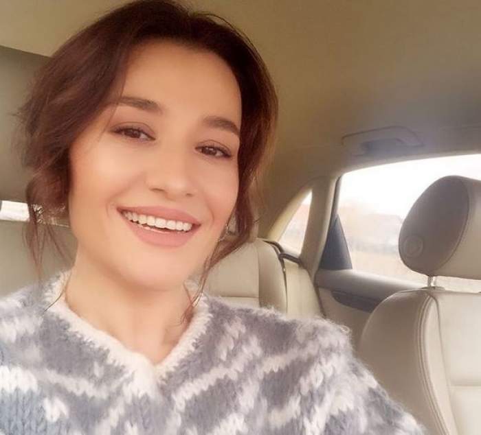 Claudia Pătrașcanu își face un selfie în mașină. Vedeta zâmbește și poartă un pulover alb cu gri.