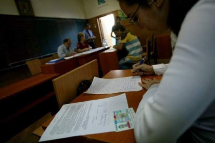 O fată care scrie pe foaie de examen, cu buletinul alături și profesori la catedră