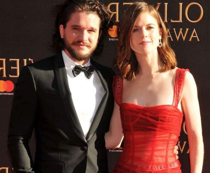 Kit Harington şi Rose Leslie se află pe covorul roșu. Ea poartă o rochie roșie, iar el un costum negru cu papion și cămașă albă.