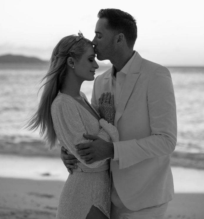 Paris Hilton si Carter Reum sunt pe plaja imbratisati, el o saruta pe frunte, ea zambeste