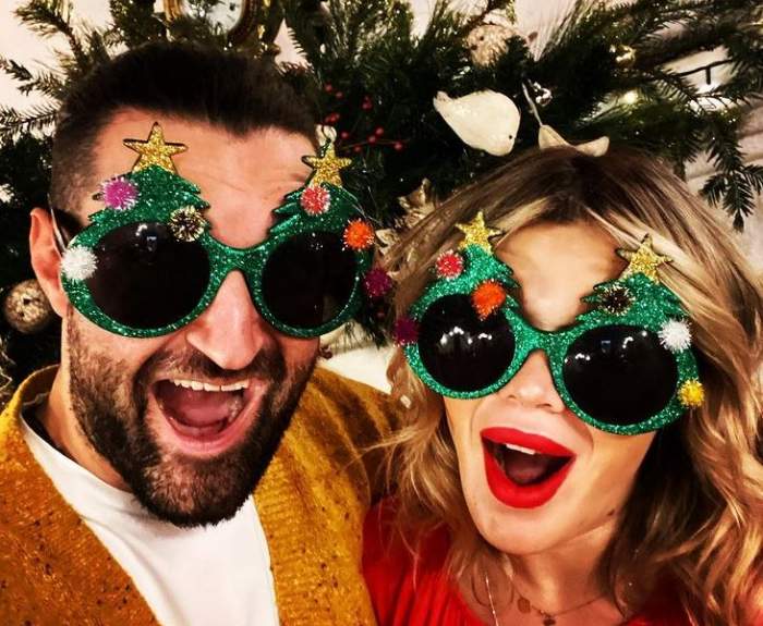 Smiley și Gina Pistol poartă ochelari de soare verzi, cu motive de Crăciun. În spatele lor este o creangă de brad. Amândoi stau cu gurile deschise.
