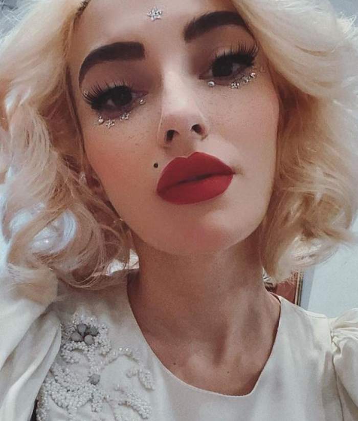 Ana Morodan își face un selfie. Vedeta poartă o bluză albă cu pietricele în formă de floare și e dată cu ruj roșu.