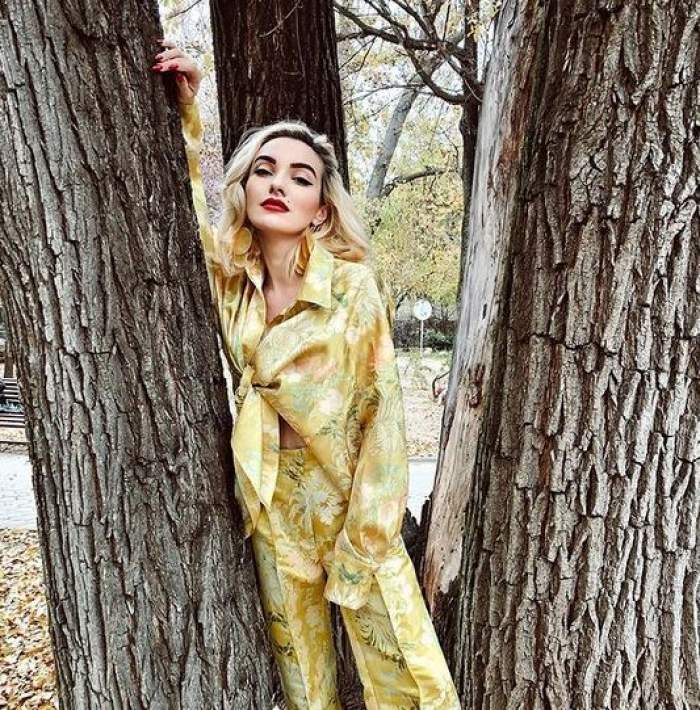 Ana Morodan e în parc, între doi copaci. Vedeta poartă un costum galben cu elemente florale verzi.