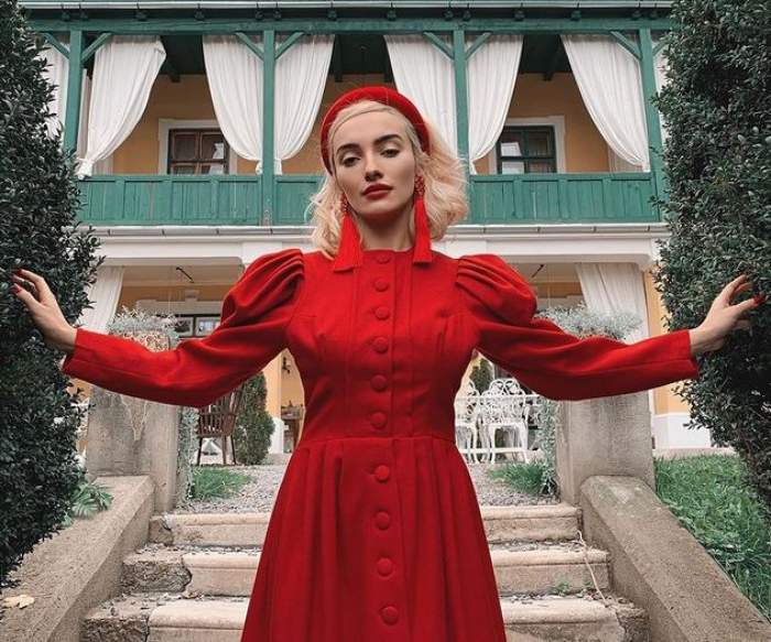 Ana Morodan e îmbrăcată într-o rochie roșie. Vedeta poartă cercei și bentiță roșie e în fața unei case.
