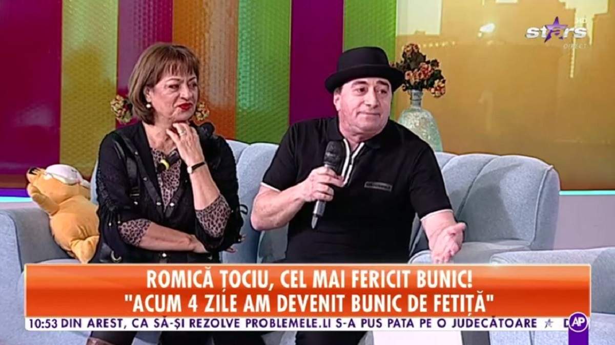 Romică Țociu și Adriana Trandafir se află pe canapeaua gri de la Star Matinal. El poartă pălărie și tricou negru, iar ea o bluză cu animal print și o alta neagră descheiată pe deasupra.