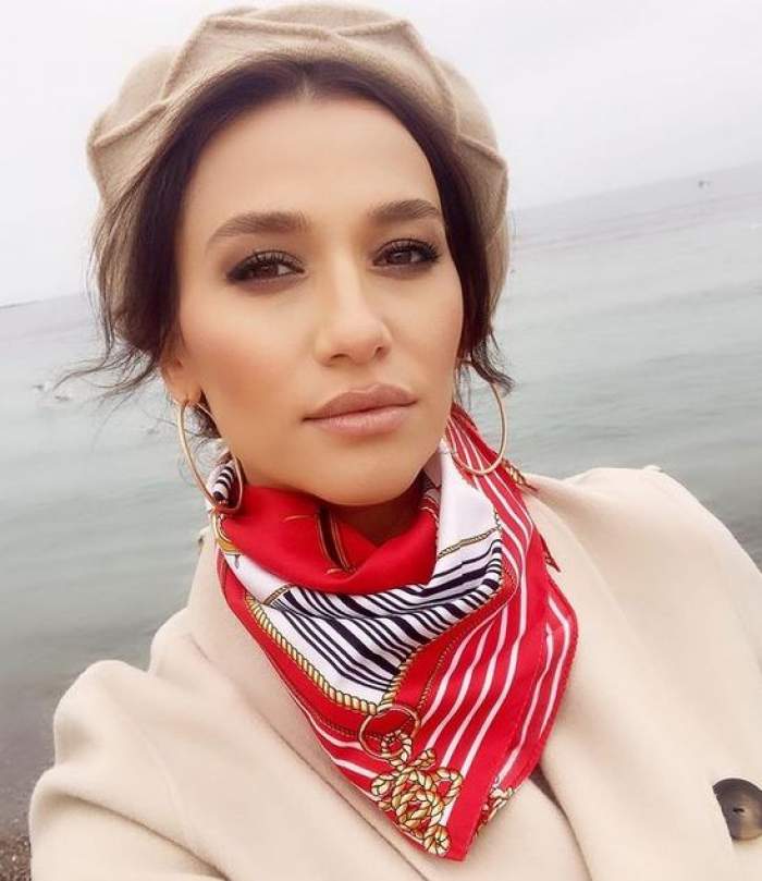 Claudia Pătrășcanu e la mare. Vedeta poartă o căciulă și un palton crem și o eșarfă roșie cu alb, nengru și auriu.