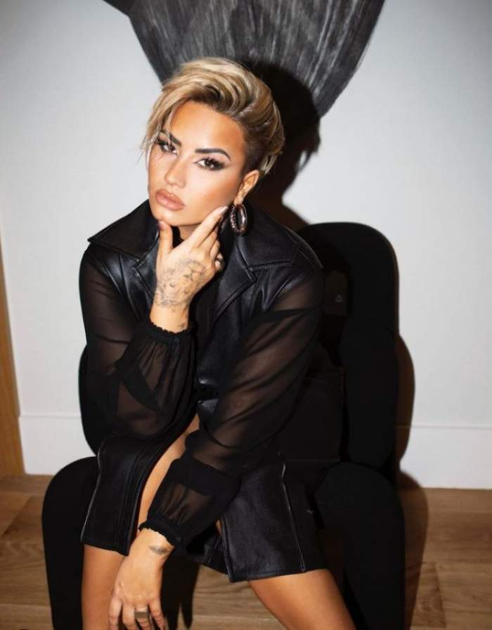 Demi Lovato poarta o tinuta neagra, sta pe un scau, este tunsa foarte scurt si vopsita blond