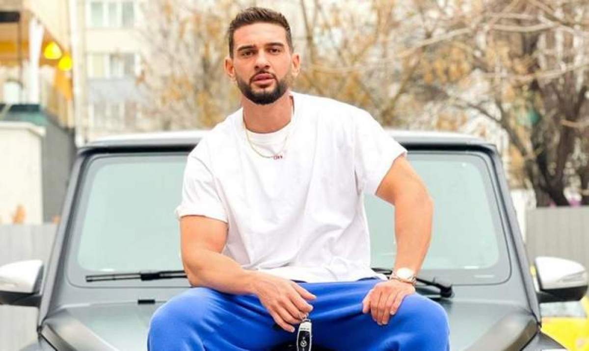 Dorian Popa, în tricou alb și pantaloni albastri, stă pe mașină