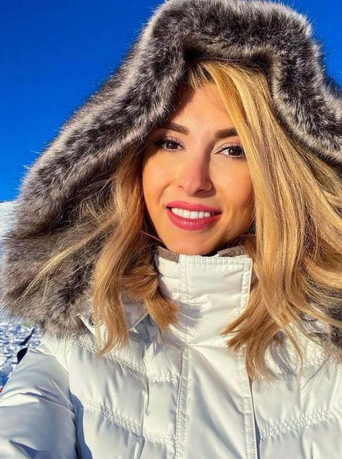 Andreea Bălan e afară. Vedeta își face un selfie și zâmbește larg. Artista poartă o geacă de iarnă albă și are gluga pe cap.