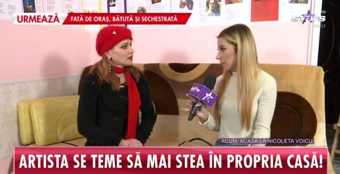 Nicoleta Voicu dă un interviu pentru Antena Stars. Vedeta stă pe o canapea maro și e îmbrăcată cu o bluză neagră. Artista poartă o căciulă și eșarfă roșie.