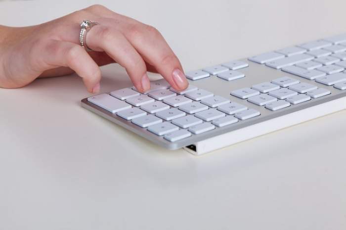 Mâna unei femei,cu inel cu diamant pe deget, butonează o tastatură albă