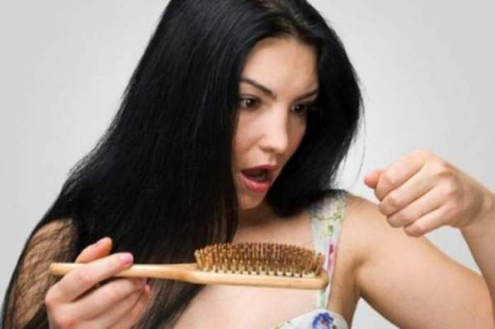O femeie mirată de căderea părului, cu peria de pieptănat  în mână
