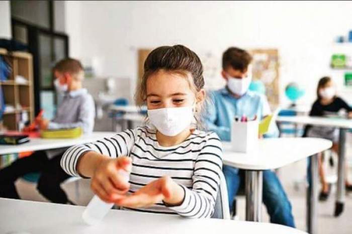 Mai mulți elevi care poartă mască și se dezinfectează