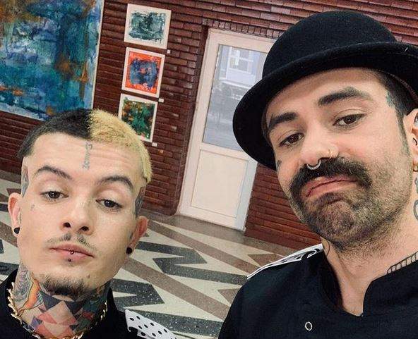 Kani și Zanni își fac un selfie. Amândoi sunt îmbrăcați cu uniforme negre de bucătar. Kani are o pălărie neagră pe cap.