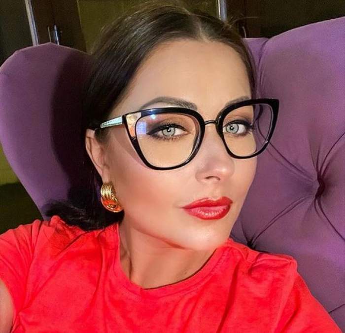 Gabriela Cristea își face un selfie. Vedeta stă pe un fotoliu mov, poartă ochelari de vedere și un tricou roșu.