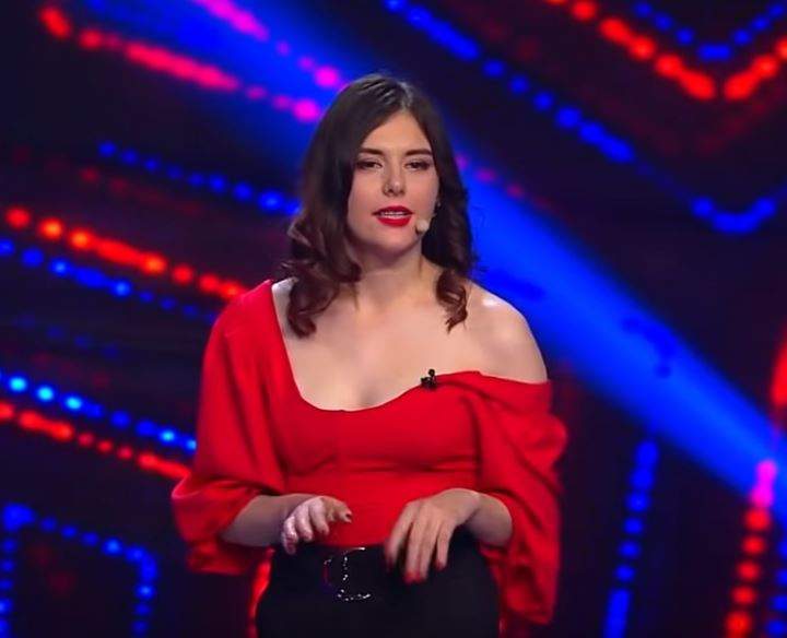 Ionela Irimescu e pe scena de la iUmor. Concurenta poartă pantaloni negri și bluză roșie.