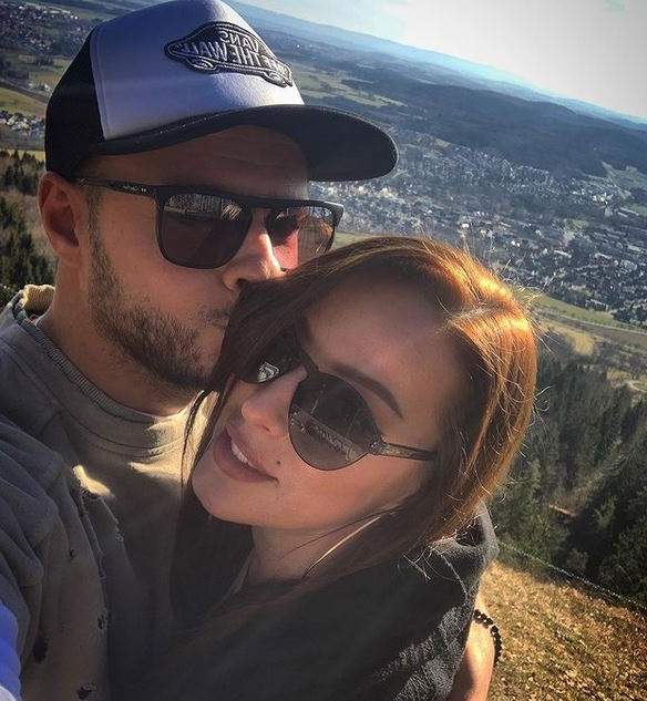 Lavinia Ilcău și iubitul într-un selfie. El o sărută pe obraz, iar ea poartă ochelari de soare și zâmbește larg. În spatele lor se vede o câmpie cu mai multe case.