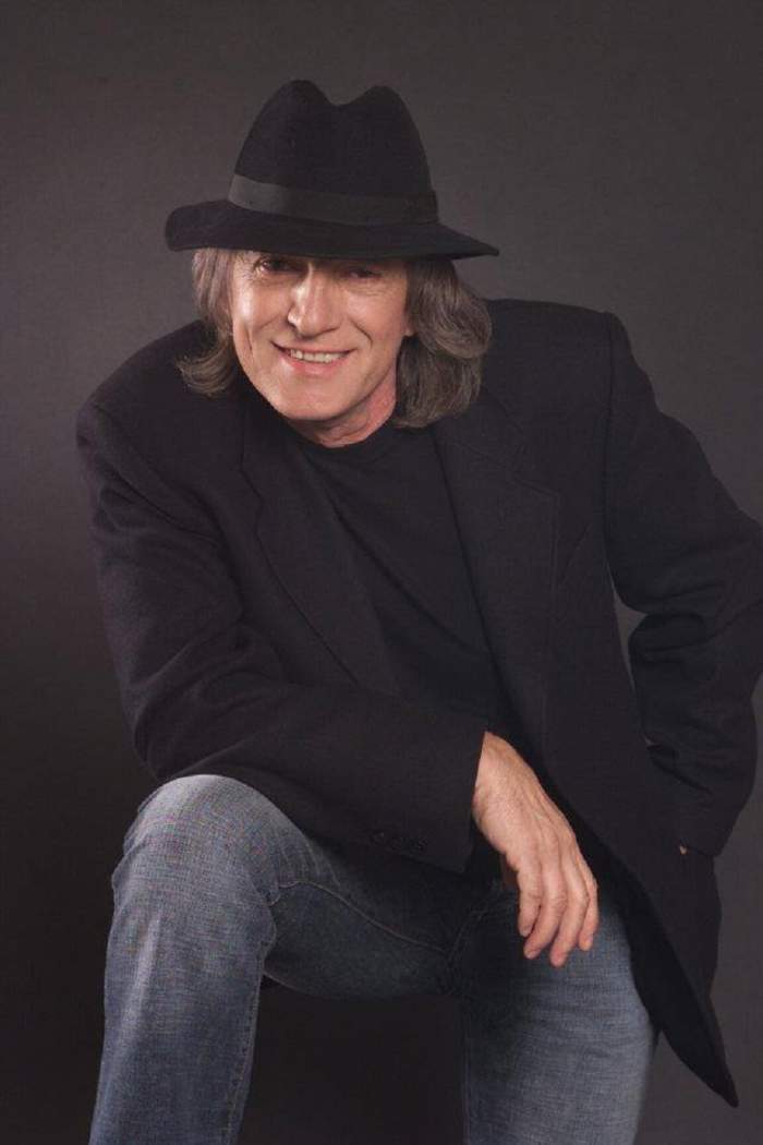 O poză cu Mihai Constantinescu de când trăia. Artistul purta sacou și pălărie neagră și o pereche de blugi albaștri.