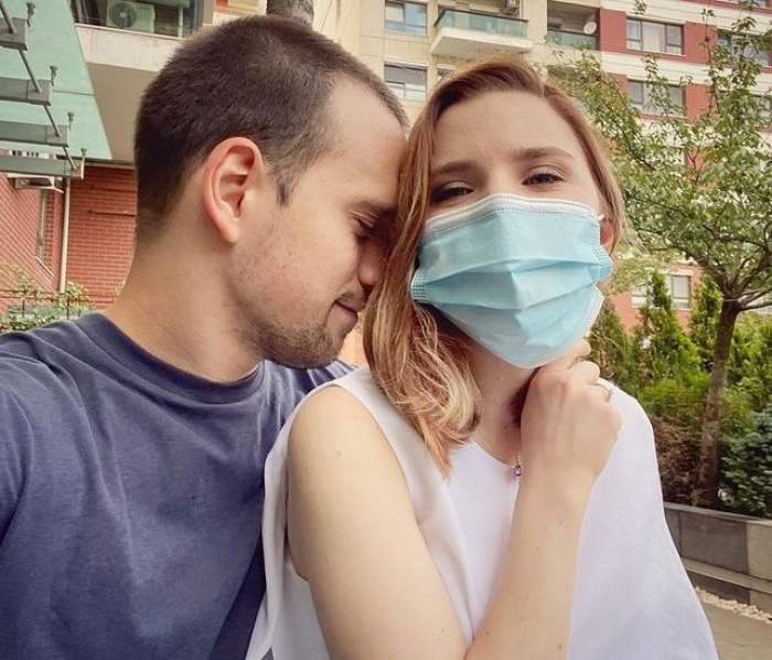 Cristina Ciobănașu și Vlad Gherman se află afară. Ea poartă mască de protecție și un maiou alb, iar el un tricou albastru și își ține fruntea lipită de părul ei.