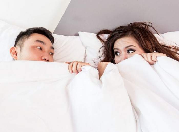Imagine simbol cu un cuplu care stă în pat. Femeia și bărbatul își țin cearceaful deasupra nivelului gurii.