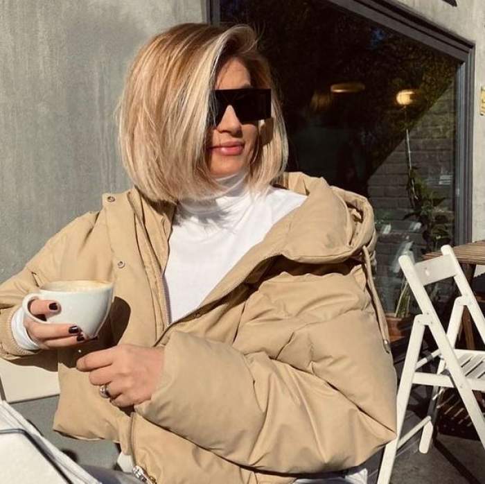 Anamaria Ionescu se află la cafenea. Vedeta poartă ochelari de soare, o geacă crem și pe dedesubt o bluză albă. Blonda ține în mână o ceașcă albă.